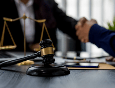 A gavel with a lawyer shaking hands with a client in the background