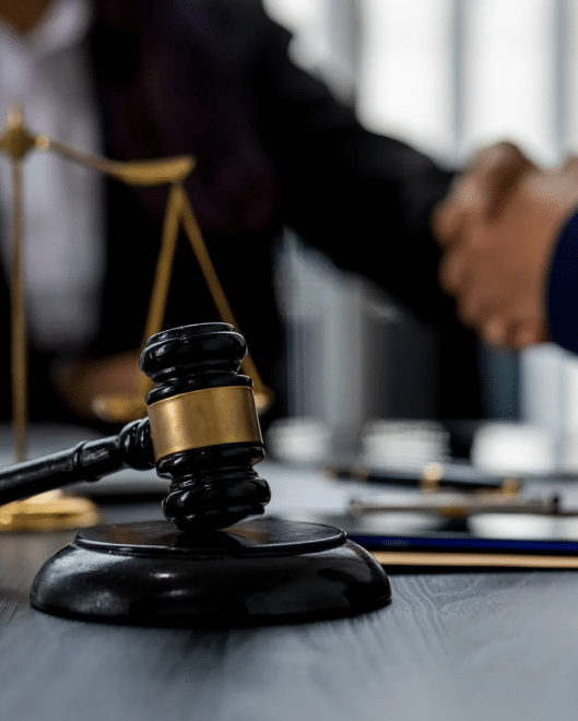 A gavel with a lawyer shaking hands with a client in the background