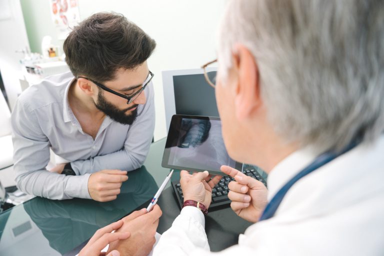 Mature Male Doctor Using A Digital Tablet For His Diagnosis.